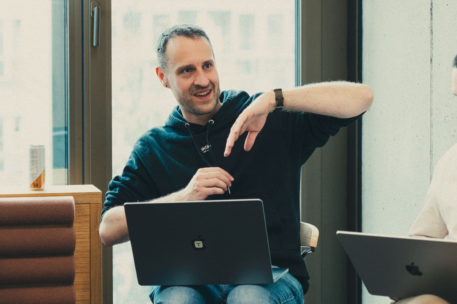 A Taktile team member talking and gesturing beside a window, with a laptop open on their lap
